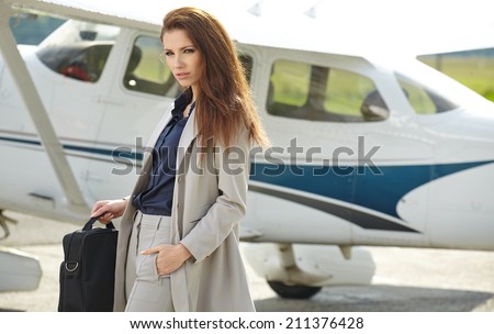 Portrait of wealthy woman with luggage walking against private jet at airport terminal