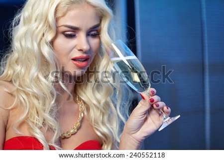 Happy and beautiful blond woman in a party red dress with a glass of champagne