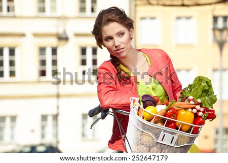Pretty spring woman with bicycle and groceries in old town street.