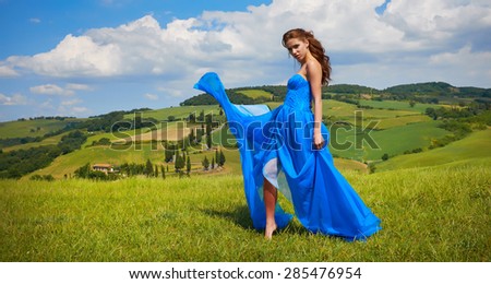 Happy woman in blue dress in green hills.