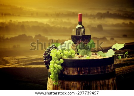 Red wine bottle and wine glass on old barrel. Beautiful Tuscany background