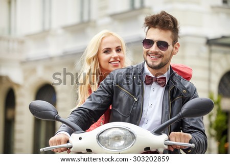 Fun ride. Beautiful young couple riding scooter together while happy woman bonding to her boyfriend and smiling