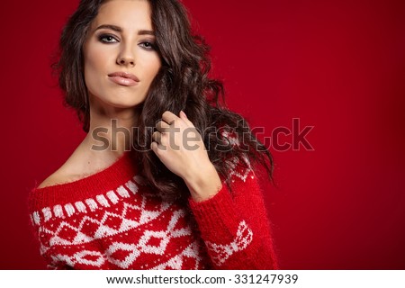 Beautiful girl in a red sweater with white ornaments stands near a red background