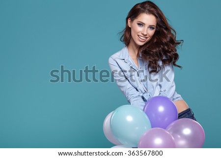 Happy young woman standing over blue wall and holding pink and white balloons. Pleasure. Dreams. Toned.
