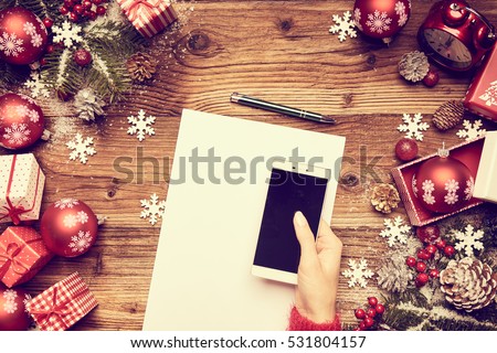 Woman using a touch screen smart phone, hands close up, top view, desktop with gifts and Christmas letters on background