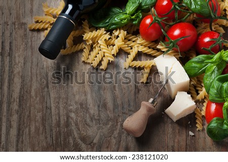 Concept of italian food with raw fusilli, tomato, basil, cheese and wine on the wooden table