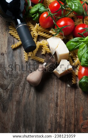Concept of italian food with raw fusilli, tomato, basil, cheese and wine on the wooden table