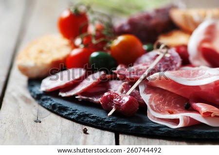Antipasto with ham, olive and tomato on the wooden table, selective focus