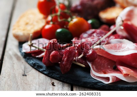Antipasto with ham, olive and tomato on the wooden table, selective focus