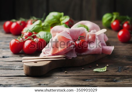 Italian traditional prosciutto with tomato and basil on the wooden table, selective focus