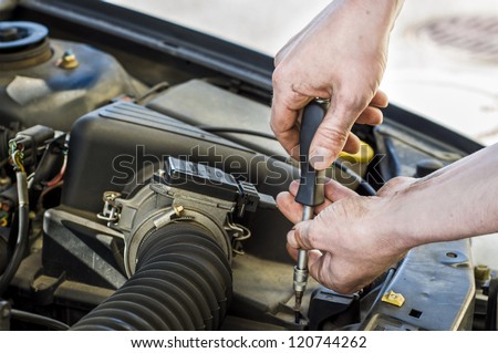 Car mechanic working under the engine hood of a car.