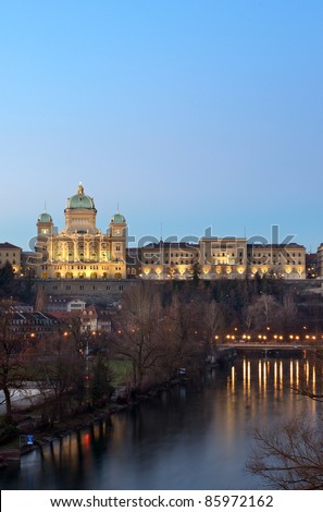 The Swiss parliament building (Bundeshaus) in Bern under a deep blue evening sky in winter. Below is the river aar (Aare).