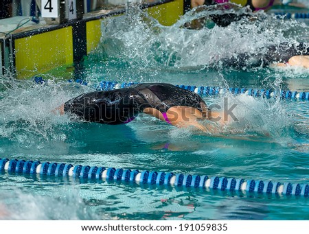 Female swimmer diving  into water at the start of a backstroke race