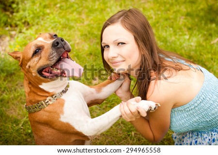 Girl playing with a dog in the park on the grass. A dog happy and stuck out her tongue, a woman holding her front paws and looks at the camera smiling.
