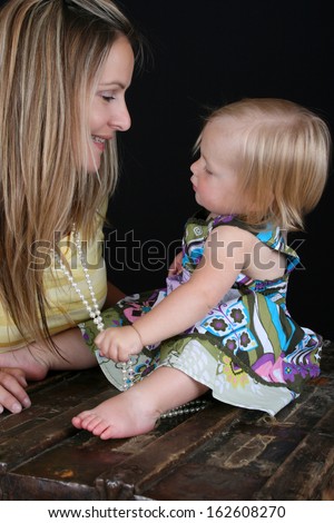 Beautiful little blond girl playing with a string of pearls around her mothers neck