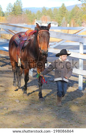 Young cowboy walking his horse on the farm