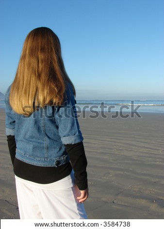 Young girl standing on the beach looking into the distance