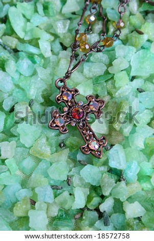 Cross shaped piece of jewelery on green bath crystals