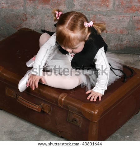 Tiny travelling ballerina sitting on a suitcase wearing a leather undercoat over her tutu