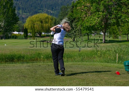 Blond female golfer following her shot from the tee-box down the fairway