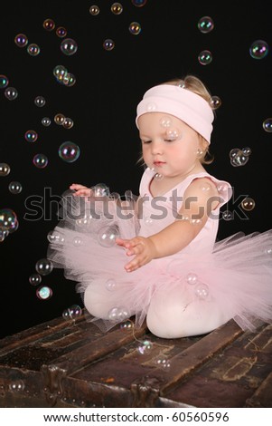 Cute blond toddler in ballet tutu reaching out to touch bubbles