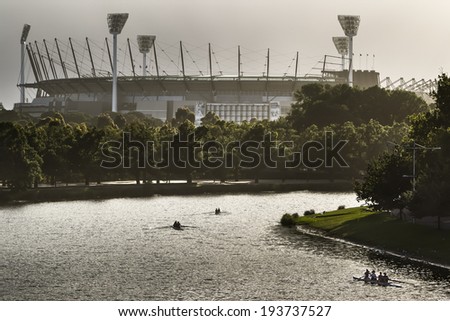 Silhouetted rowers on the Yarra River with the Melbourne Cricket Ground in the background Silhouetted rowers on the Yarra River with the Melbourne Cricket Ground in the background