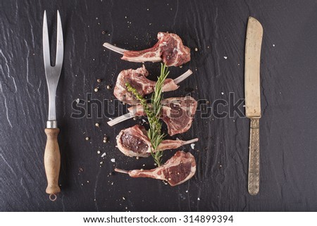 Rack of lamb, Raw rack of lamb cut in pieces decorate and seasoning with rosemary tomato herbs and olive oil fork and knife on black stone