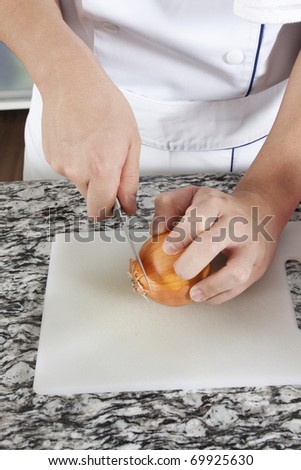 Cutting onion, Chef cutting onion with a knife on the chopping plate in a granite topped kitchen.