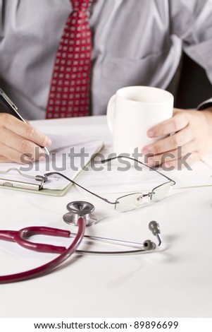 working doctor, a doctor in red tie write down on the note board while grab coffee cup.