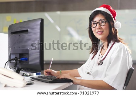 Christmas doctor, Female Asian doctor with Christmas hat and stethoscope working on computer.