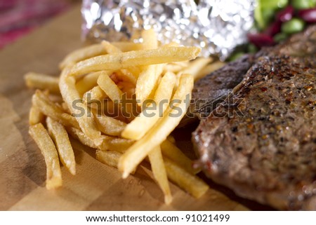 Fries, thin French fries on steak dish served on wood plate.