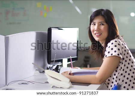 Office work, Asian girl at busy office smiling in front of computer.