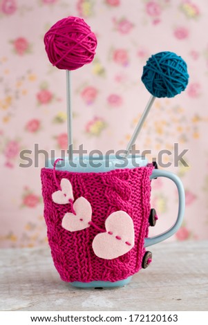 Blue cup in pink sweater with felt hearts with ball of yarn