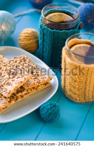 Two cups of delicious tea in knitted sweater yellow on blue background and cookies