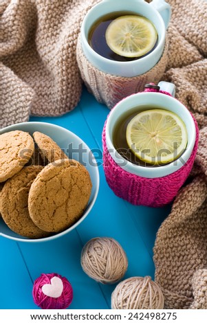 Two blue cup of tea in knitted sweater with hearts felt standing next to tangle bright filaments and blanket knitted on blue background
