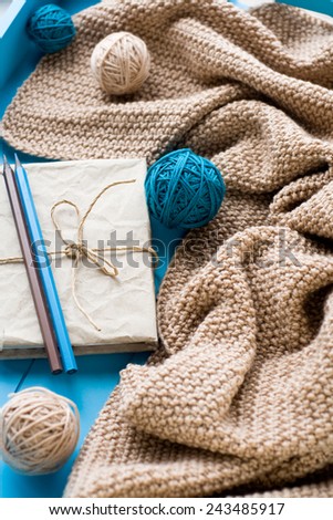 One old notebook in knitted cover lie next to the coil bright filaments and blanket knitted on blue background