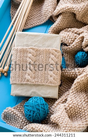 Old notebook with knitted wrap, beige knitted blanket and spokes lie on blue background
