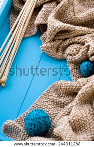 Wooden needles lie next to the bright tangle of threads and knitted blanket on blue background