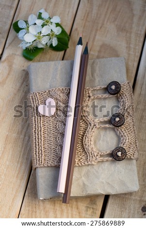 Old vintage notepad Knitted sweater in beige, heart from felt and pencils on wooden background.