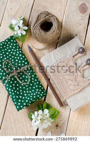 Old vintage notepad knitted in beige sweater, thick skein of yarn, cloth, pear blossom, pencil lying on the unpainted wooden background.