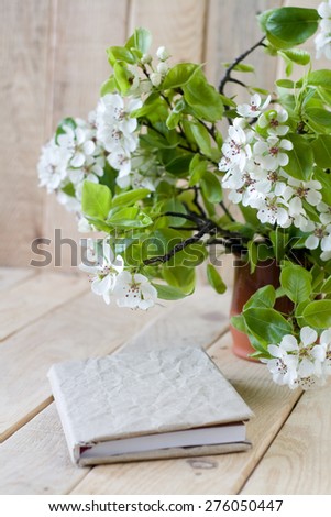 A bouquet of flowering branches of fruit trees and an old notepad on unpainted wooden background