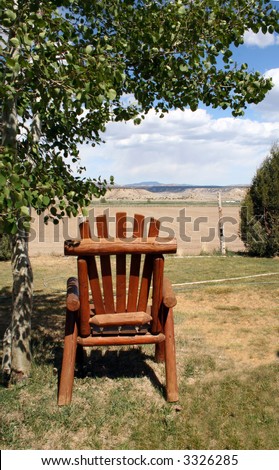 Wooden lawn chair, under a tree, overlooking the mountains in the distance.