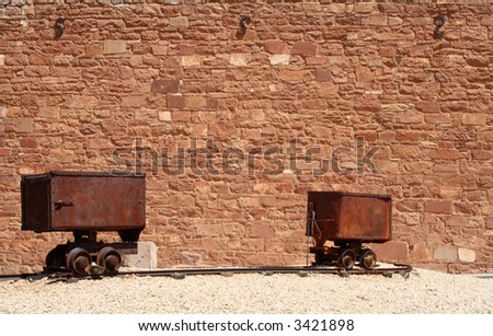 Two rustic, rusted, vintage rail ore cars outdoors in front of an old brick wall in the desert southwestern U.S.