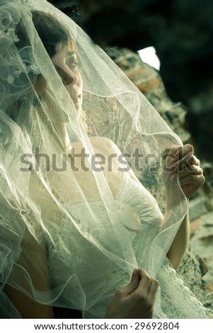 Bride looking sad, holding her veil, in the ruins of a church