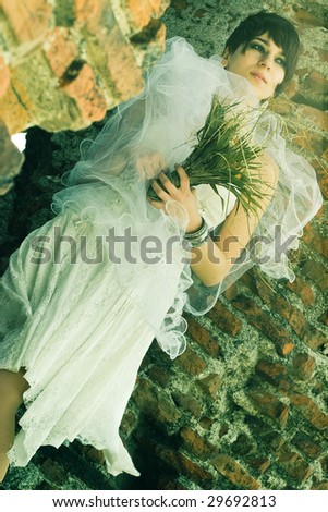 Bride looking sad with her veil and bouquet in her hands, in the ruins of a church