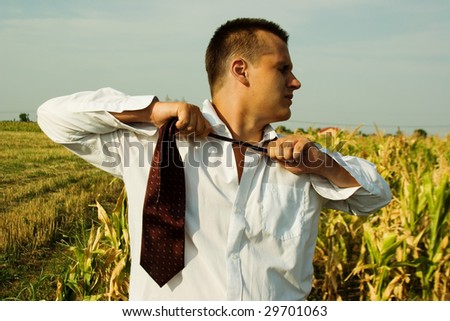 Business man in a corn field, untying his tie, seeking freedom from city life and workload
