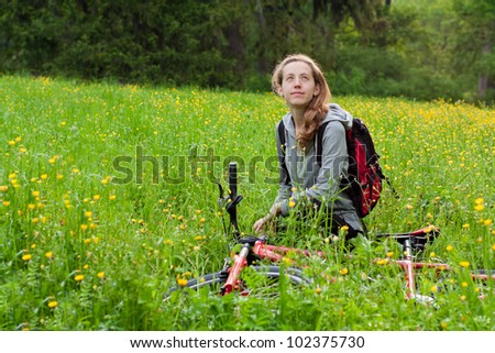 Happy woman cyclist with bike and backpack among of green blooming nature in spring