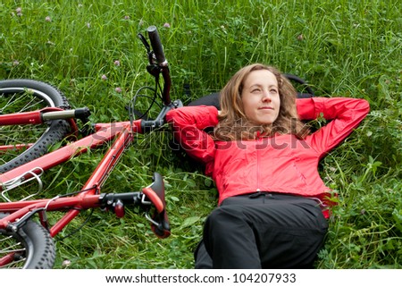 Happy woman cyclist with bike in a red tracksuit relaxes lying among of green grass on the nature. Outdoor