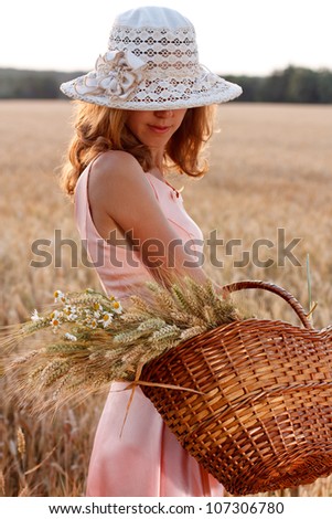 Elegant  romantic woman in hat with basket full of ripe wheat ears and daisies in the wheat field on a summer evening