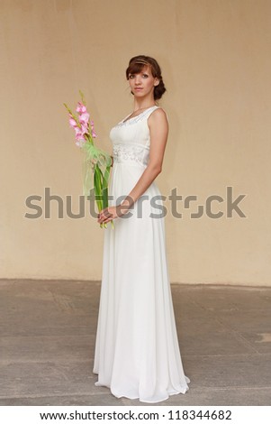 Portrait of beautiful greek woman posing in white dress with pink flowers in her hands